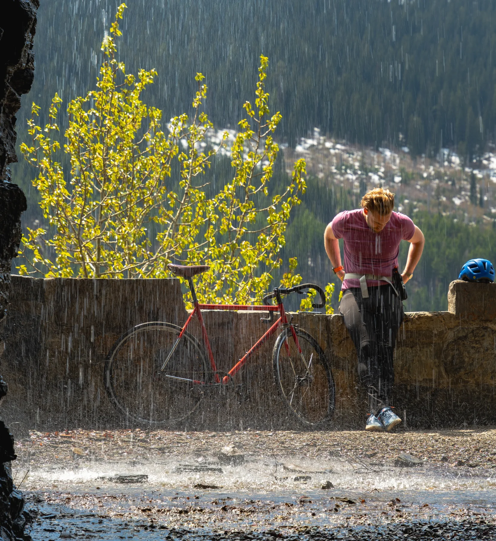 Charlie standing beside a red road bike in a mountain downpour